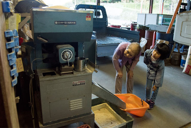 籾摺り作業を覗き込む娘とお母さん