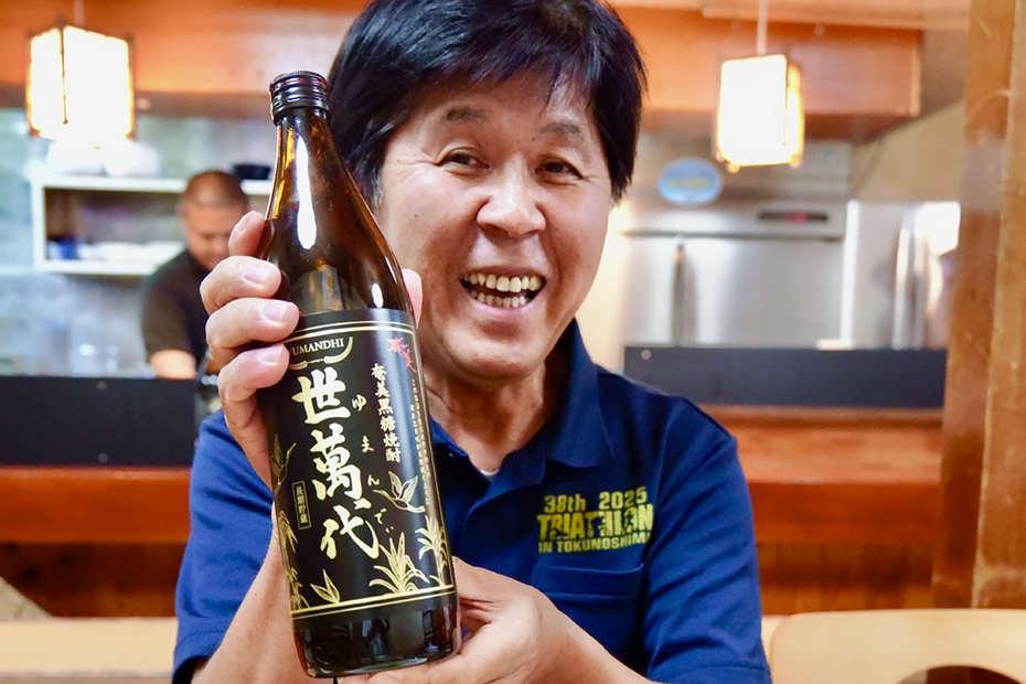 徳之島の情報発信の立役者で有名人の丸野清さん。この島のことを萬代の世に遺していきたいと徳之島産黒糖焼酎「世萬代」を片手に語る。YouTubeチャンネル「徳之島テレビ」にて島の情報を配信中。