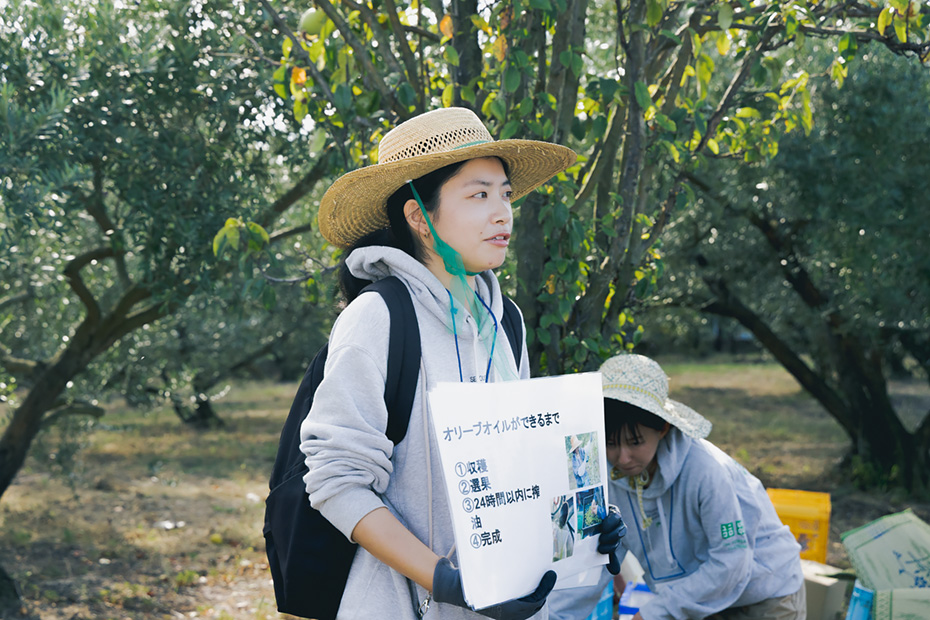 オリーブ収穫祭で参加者へオリーブオイルができるまでの工程を説明する塩川さん。オリーブの維持管理には地元の方との密なコミュニケーションが欠かせない